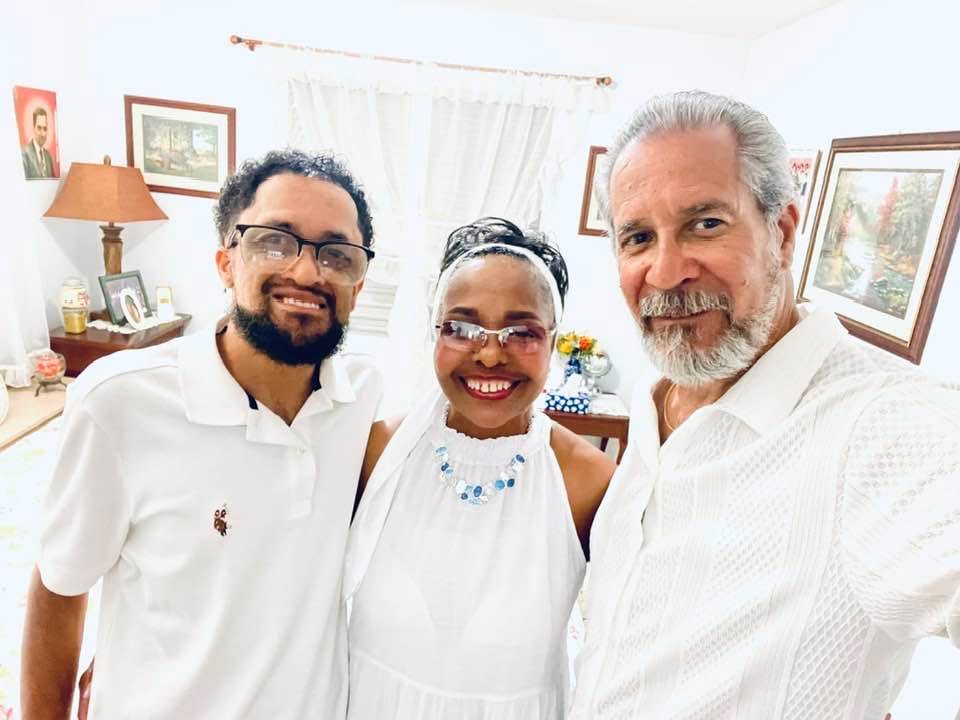 Three people smiling together indoors, dressed in white.